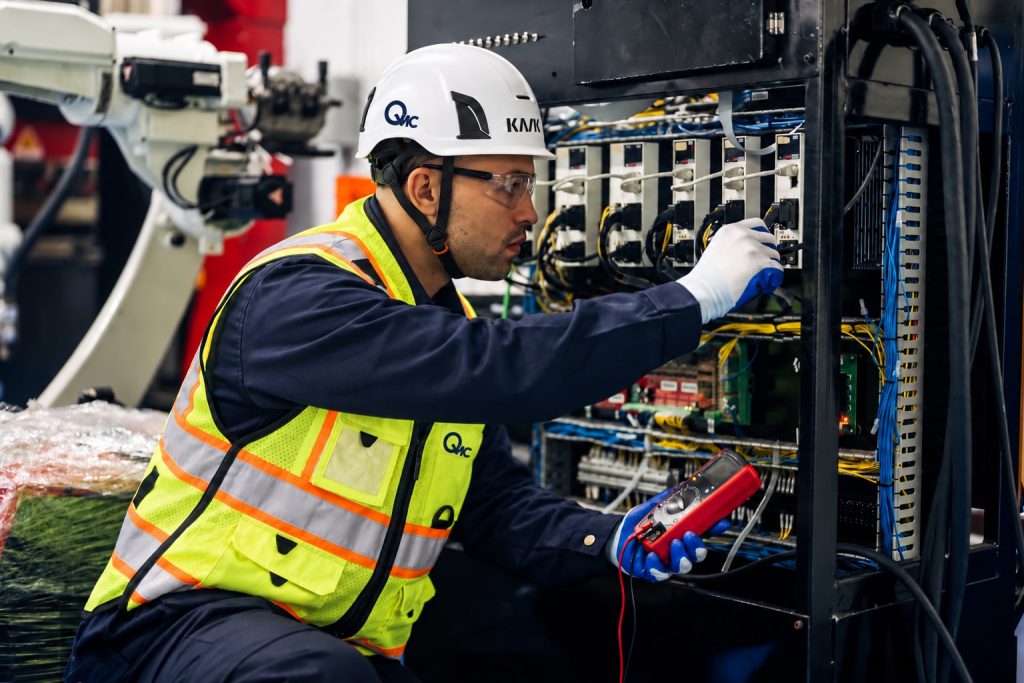 Technician inspecting an electrical control panel while holding a multimeter.